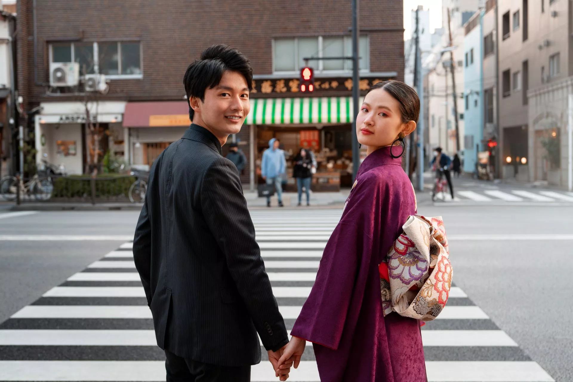一對年輕男女穿著正式服裝與紫色和服，牽手站在日本城市街道斑馬線前回眸微笑，呈現浪漫約會、成熟陪伴與包養關係中的安全感氛圍。