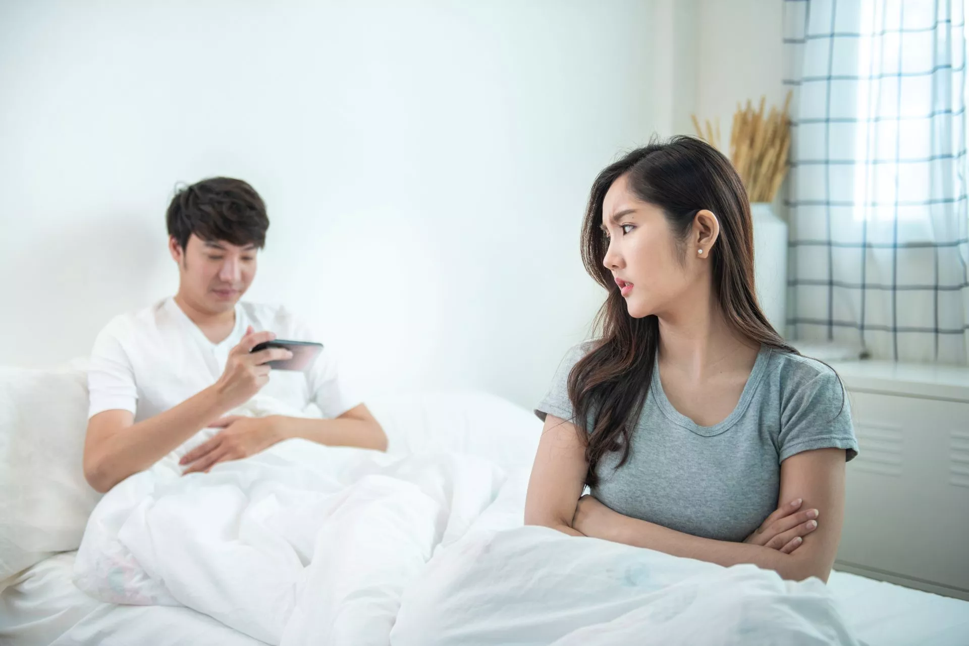 202607272637.webp 一對成年男女坐在床上氣氛緊張,女子雙手抱胸表情不悅,男子低頭看手機,呈現包養關係中的冷淡、疏離與情緒衝突情境